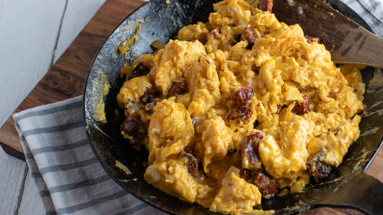Savory breakfast with scrambled eggs and fried chorizo in a black bowl on a striped napkin laid out on a wooden countertop