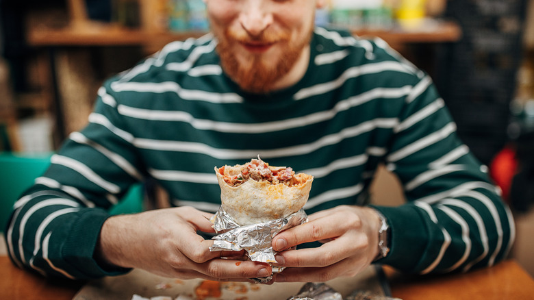 Man with a beard wearing a blue and white-striped shirt eating a burrito