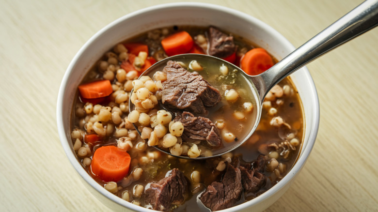 Beef and barley soup in a white bowl with a spoon
