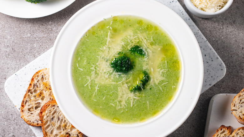 Broccoli cheese soup in a white bowl with small slices of rustic bread on side
