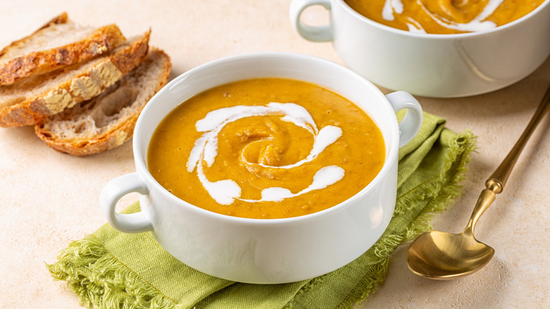Butternut squash soup in a white bowl topped with a swirl of cream next to slices of sourdough bread