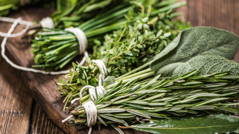 Freshly cut herbs tied together in bunches on a wooden table, like rosemary, sage, and thyme