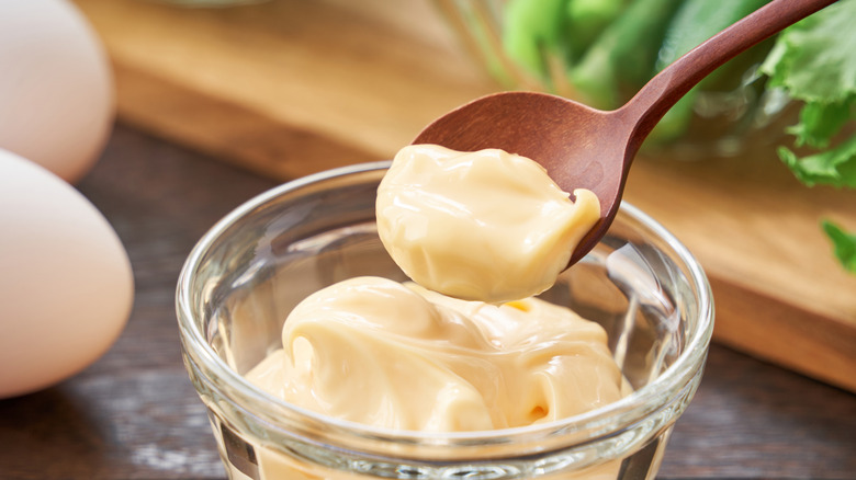 A wooden spoon scooping some fresh mayonnaise from a glass bowl