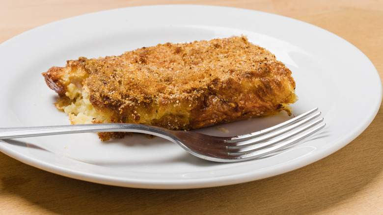 Slice of baked potato and ham with golden breadcrumb crust served in a ceramic plate with a fork.