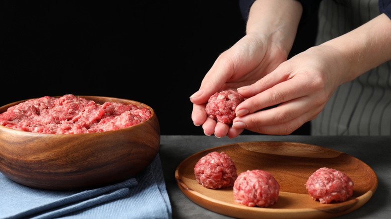 Woman making meatball from ground meat at grey table