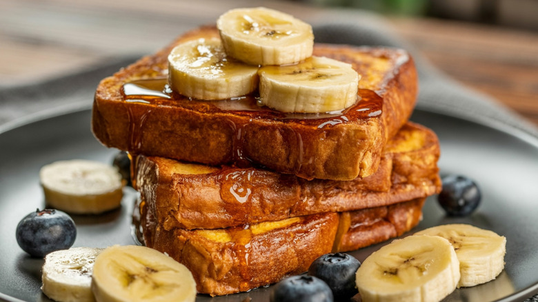 French Toast Stack : breakfast food, french toast, banana slices, syrup drizzle, blueberry garnish, rustic white plate