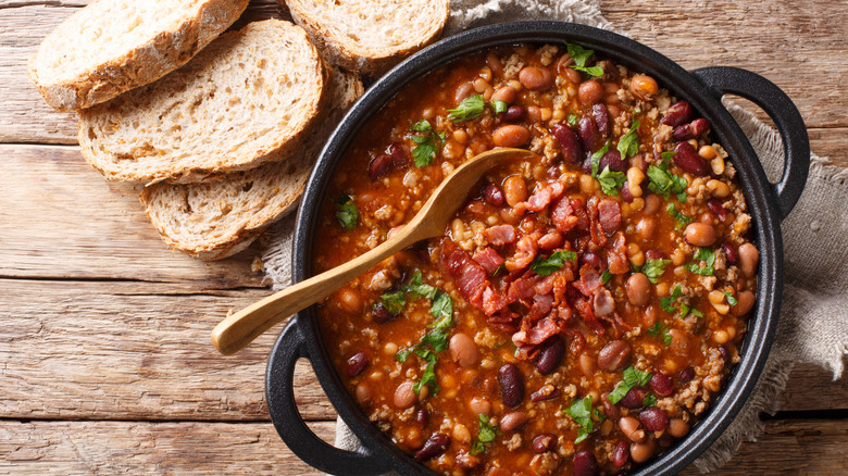 Beans and meat in a pot with a wooden spoon, next to slices of bread