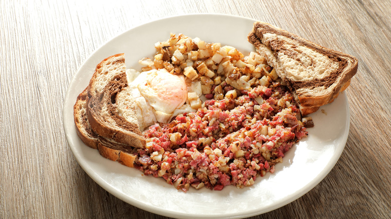A plate of corned beef hash with eggs and marble rye toast
