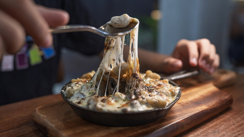 A close-up of a spoon pulling a stretchy spoonful of mac and cheese from a cast iron pan
