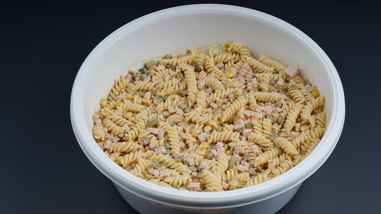 Pasta salad with diced ham and other ingredients in a white bowl on a dark background