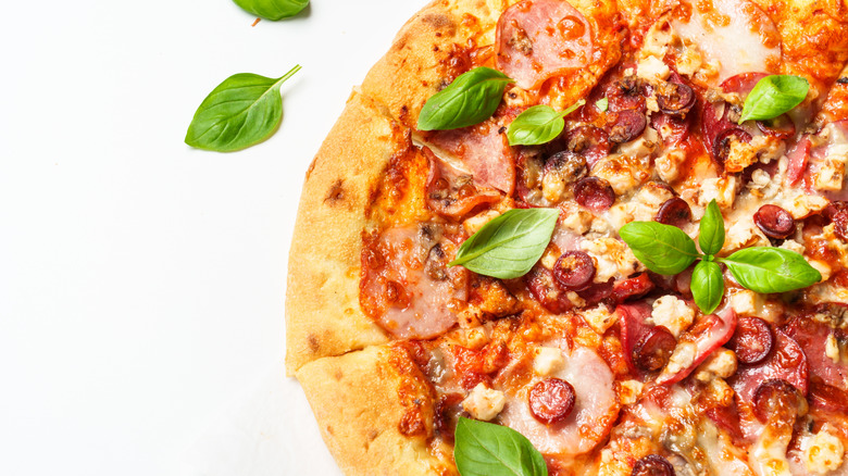 A pizza with salami, ham, and sausage garnished with fresh basil on a white background