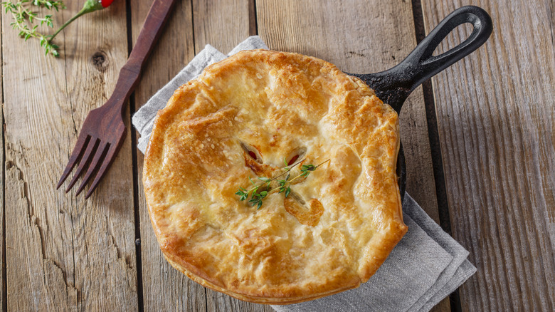 An overhead shot of an individual pot pie in a cast iron pan next to a fork on a wood table