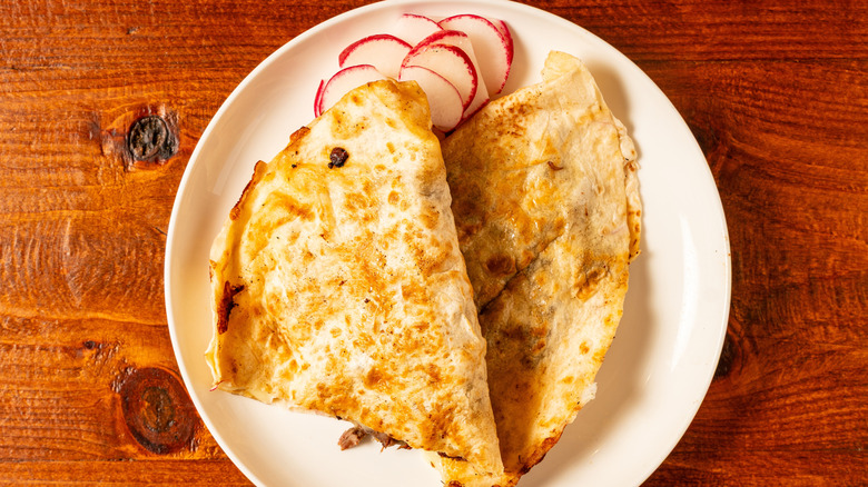 A quesadilla garnished with radish slices on a white plate on a wood table