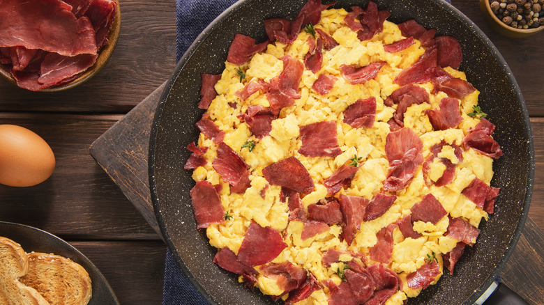 Scrambled eggs and salami on a plate next to the ingredients