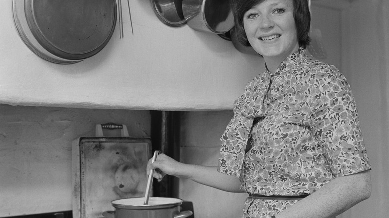 A woman cooking in a kitchen and looking at the camera, mid-1970s