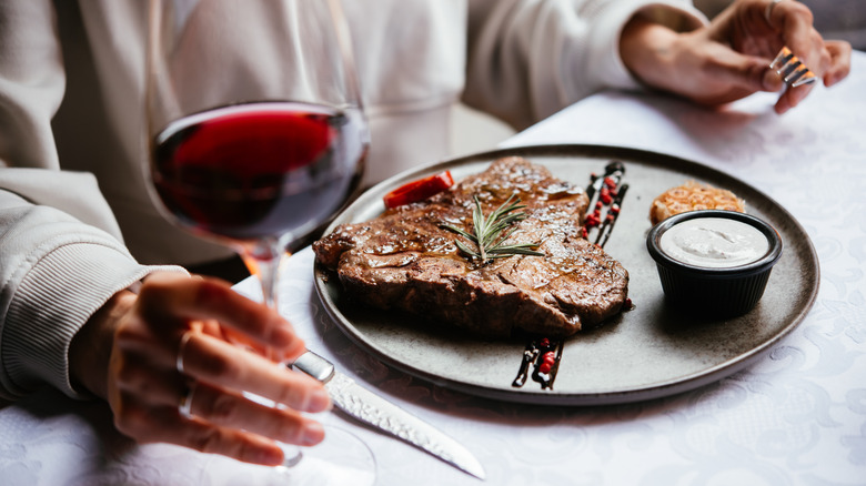 Woman holding glass of red wine next to plate of steak