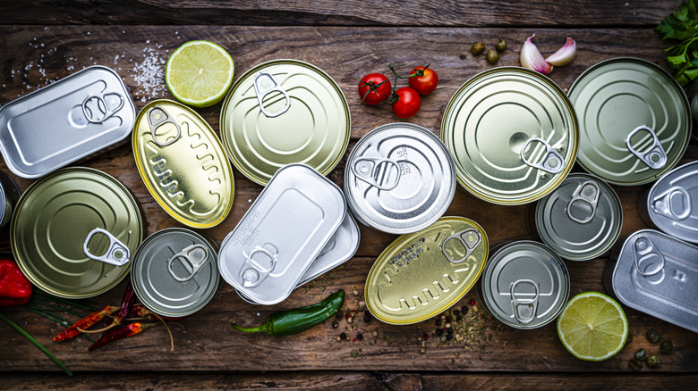 canned good variety on wooden table surrounded by produce and spices