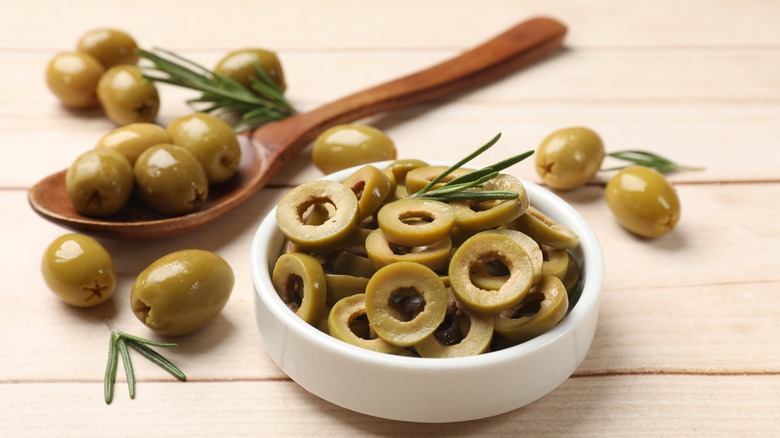white ramekin of sliced olives by wooden spoon and whole olives