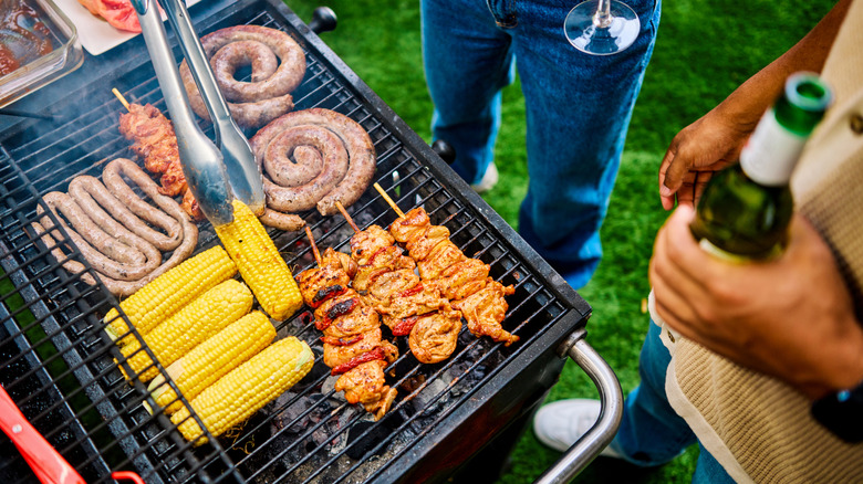 Tongs flipping corn on grill filled with sausage