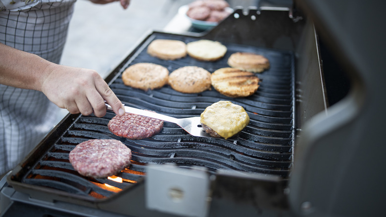 Hand with spatula flipping burgers on grill