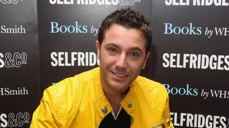 Gino D'Acampo smiles at the camera while wearing a yellow jacket