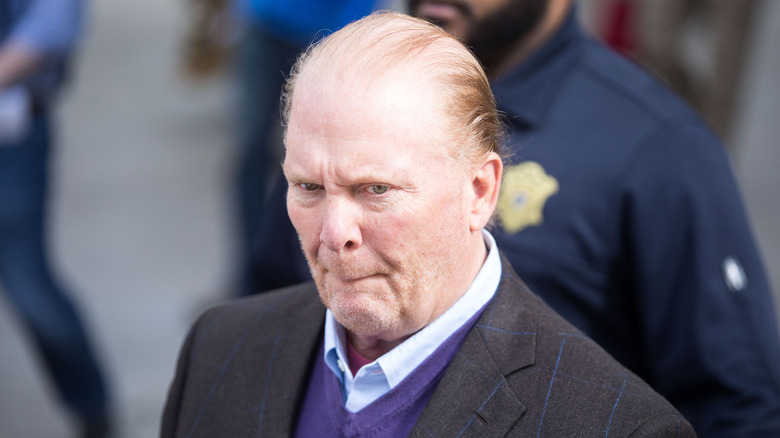Mario Batali wearing a suit and biting on his lips as he leaves court