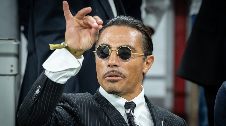 Salt Bae miming his signature salting technique in a black pinstripe suit