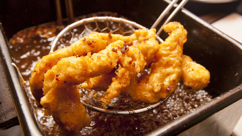 Chicken tenders being dipped in a deep fryer