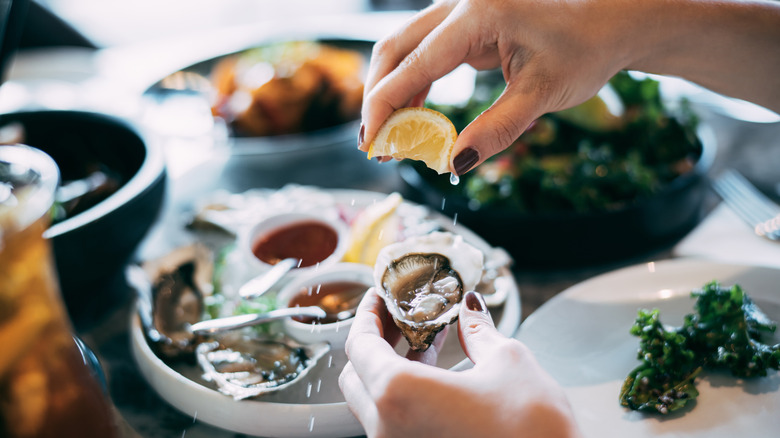 A hand squeezing lemon juice on to a fresh oyster