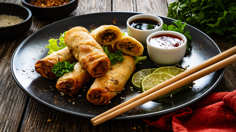 Spring rolls and sauces on a black plate on a wooden table