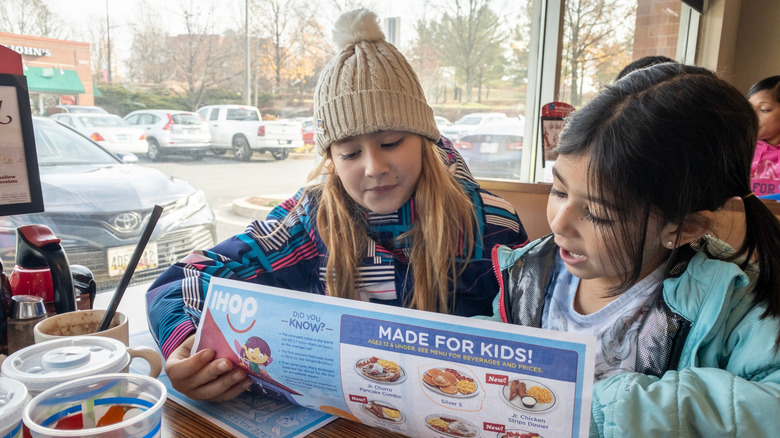 Two young girls reading IHOP menus at the table