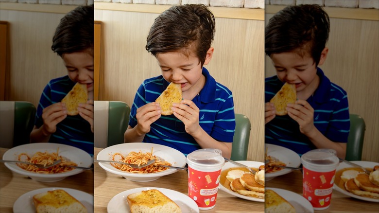 A young boy biting garlic bread with his eyes closed at a Denny's table