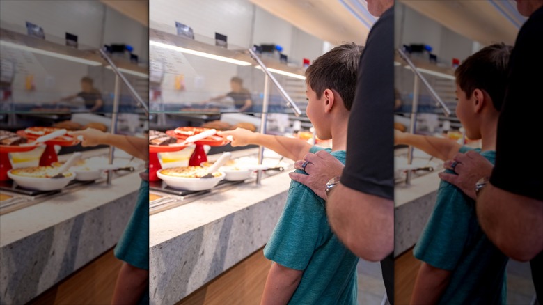 A boy choosing food at a Golden Corral buffet line alongside his parent