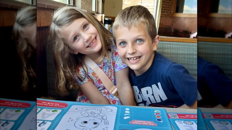 Two kids smiling at a Perkins restaurant booth seated at the table with kids menus