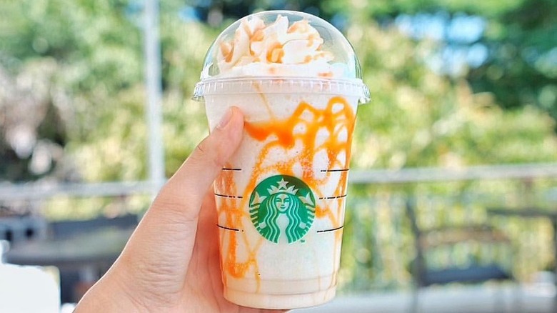 Hand holding Starbucks Butterbeer Frappuccino with blurred trees in the background