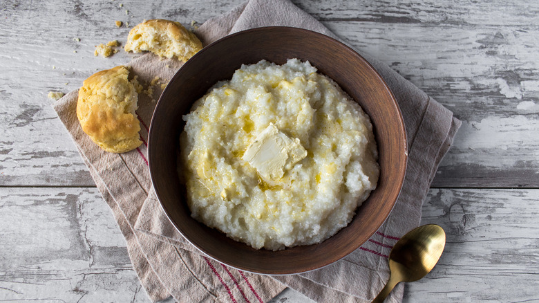 Bowl of grits with butter, biscuit, and spoon