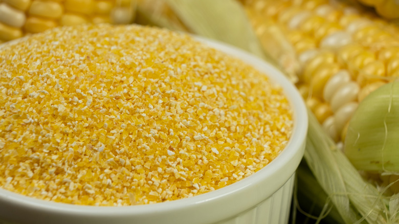 Bowl of uncooked grits next to raw corn