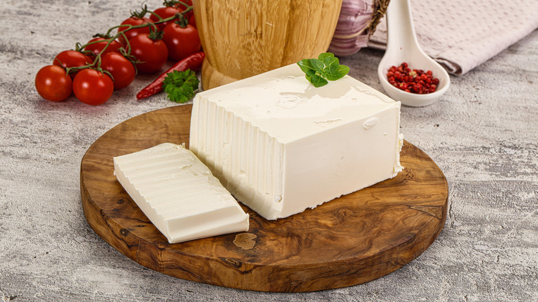 A wooden tray with a sliced slab of Feta cheese on it.