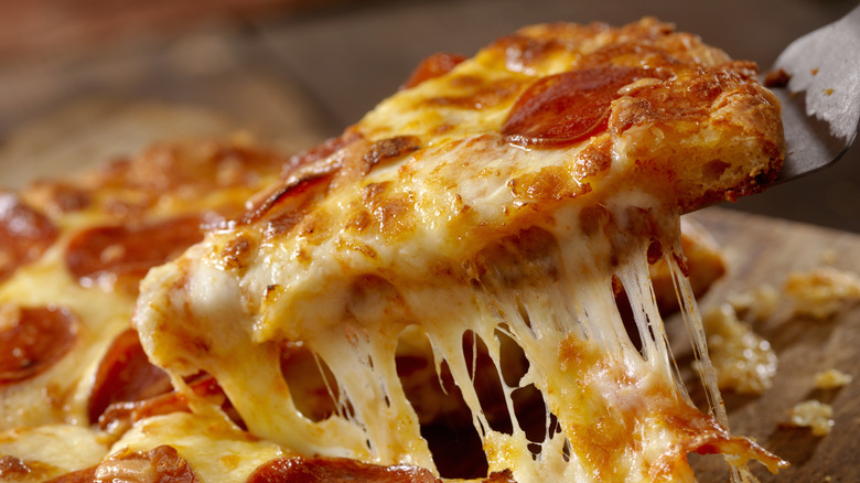 A slice of pepperoni pizza being lifted from a pizza.