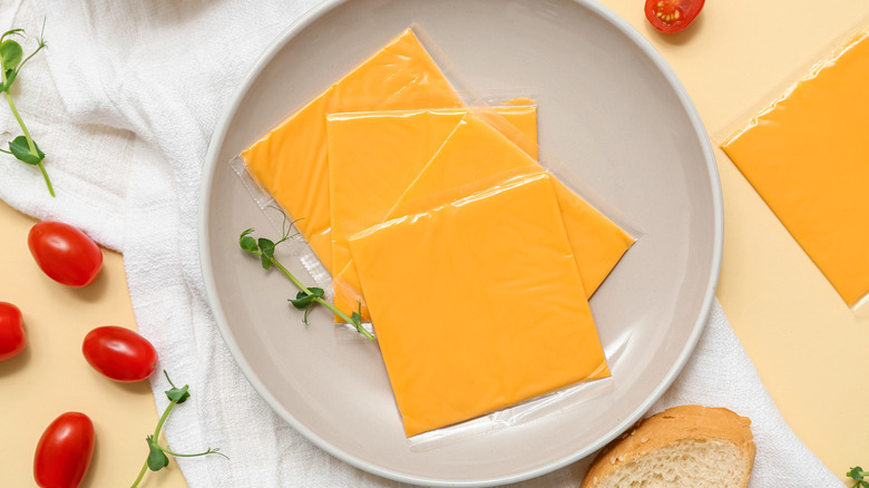 A plate with three slices of plastic-wrapped American cheese on it.