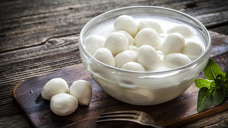 A bowl full of water and small balls of fresh mozzarella cheese.