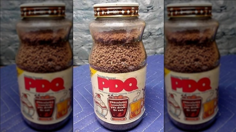 A full, clear glass PDQ jar; lid is brown with a star design on it, PDQ beads are visible; label says "PDQ" in red block letters with drawn sundae on the left, a chocolate drink in the center, and a hot drink on the right