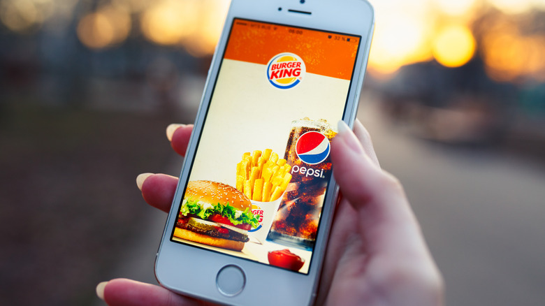 Hand holding a phone displaying the Burger King app outdoors