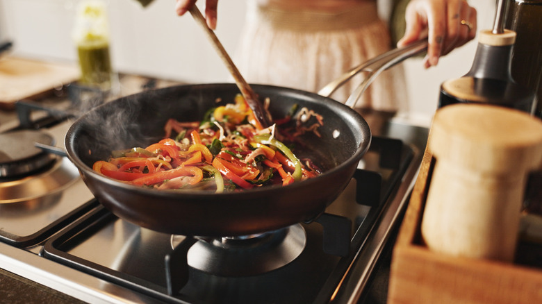 Person pushing stirfried vegetables around pan with wooden spoon