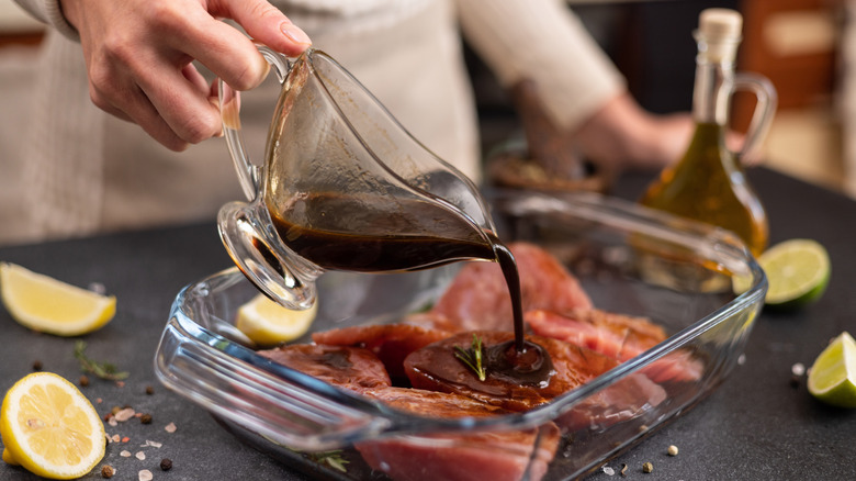 Hand pours sauce onto meat in glass tray