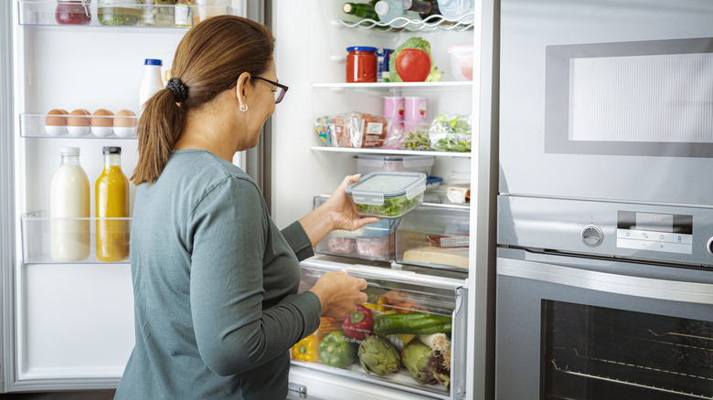 Woman putting a tub of green vegetables in the refrigerator