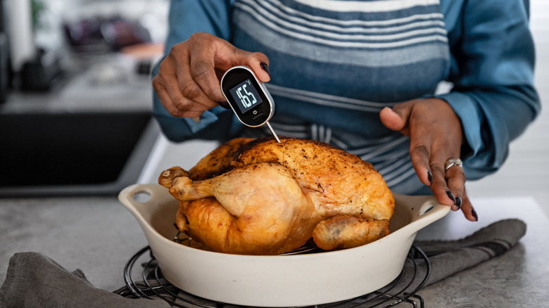 Woman measuring chicken temperature with meat thermometer