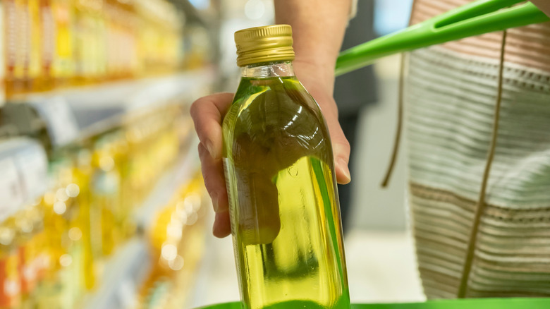Shopper placing bottle of cooking oil in basket at store