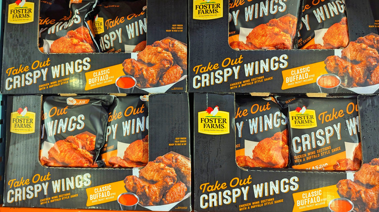 Bags filled with Foster Farms take out crispy wings rest in stacked cardboard boxes in a Costco warehouse.