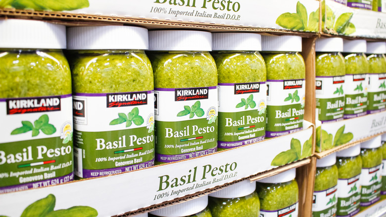 A row of jars filled with Kirkland Signature basil pesto rest in the cardboard packaging.